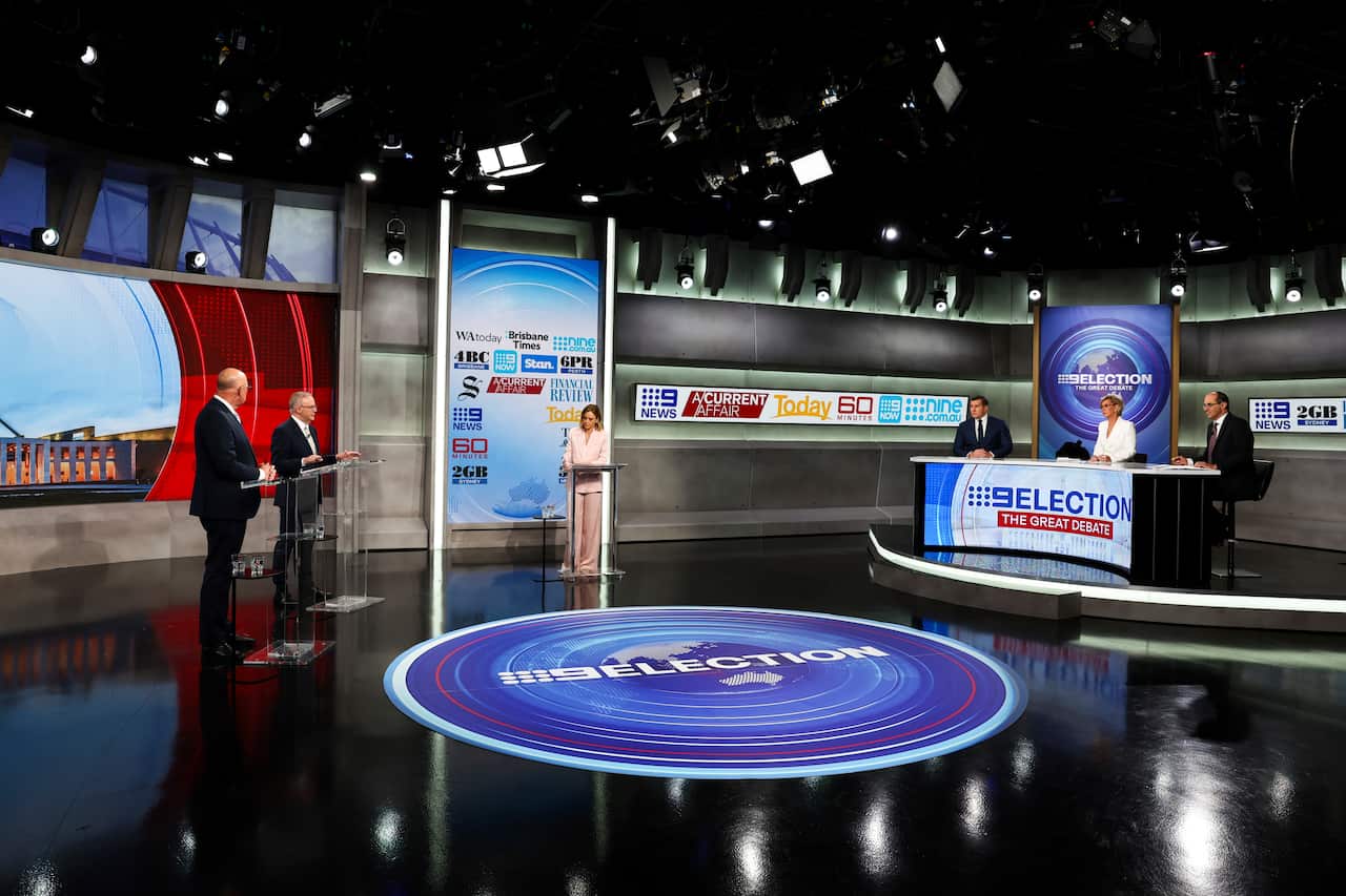 The leaders stand at separate lecterns facing a desk of three panel members. 