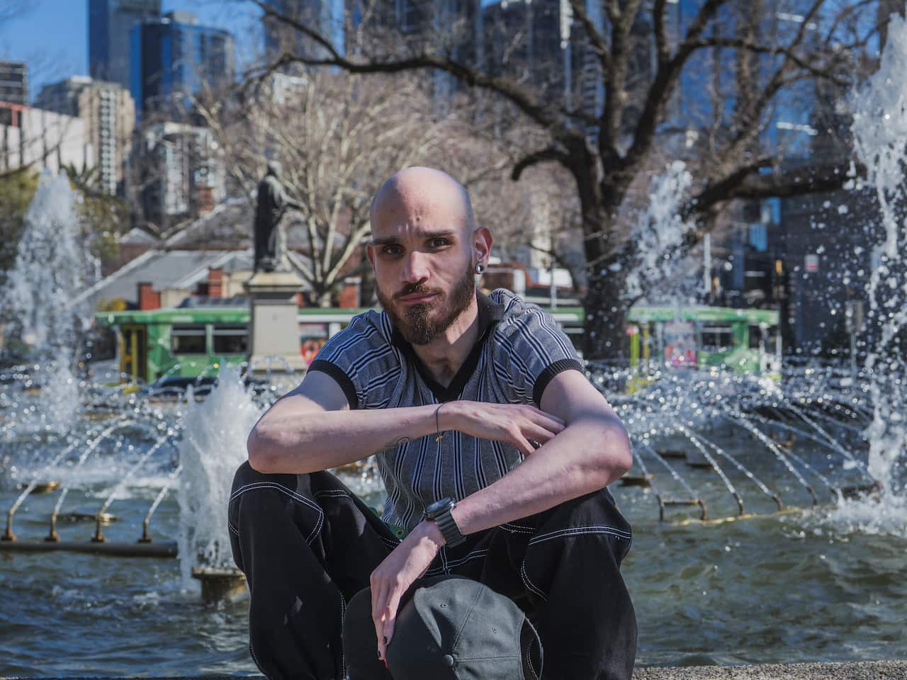 A man sits in front of a water fountain in a park. 
