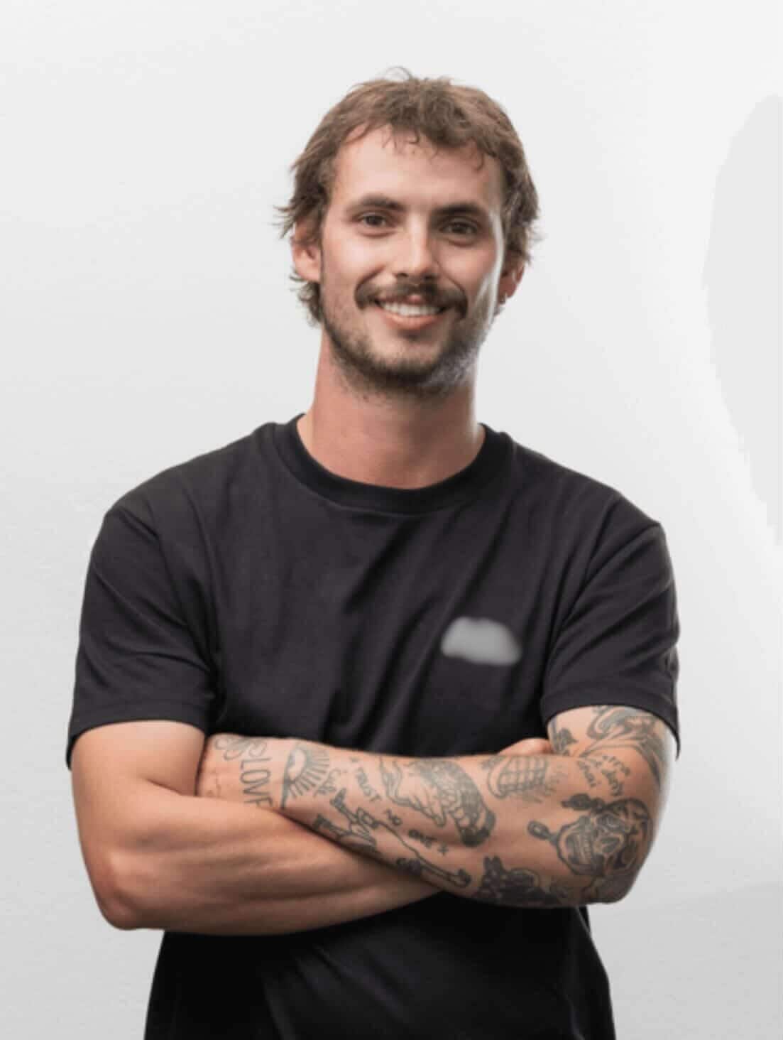 A man with tattooes crossing his arms and smiling.