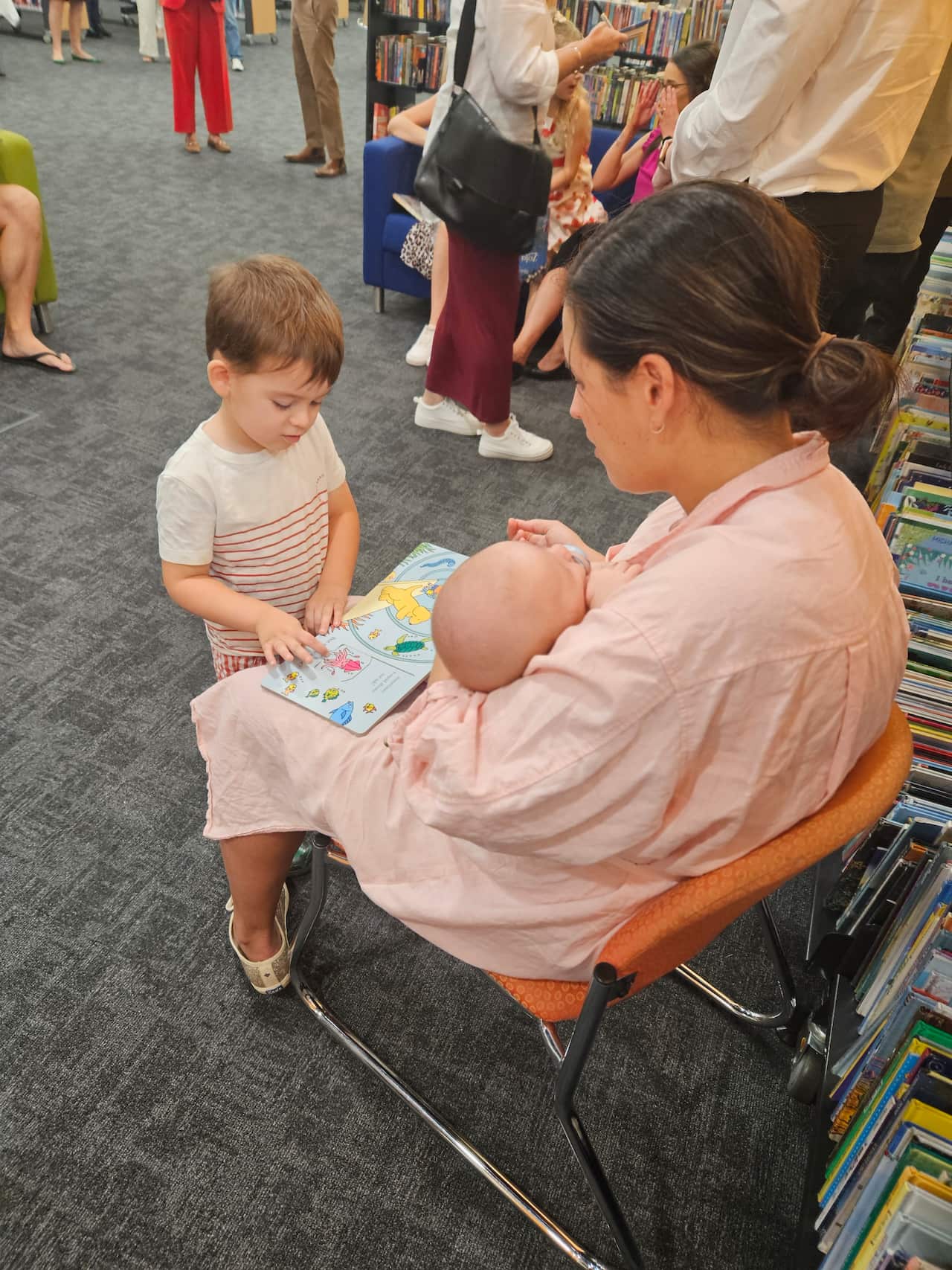 A woman reading to her child while holding a baby.
