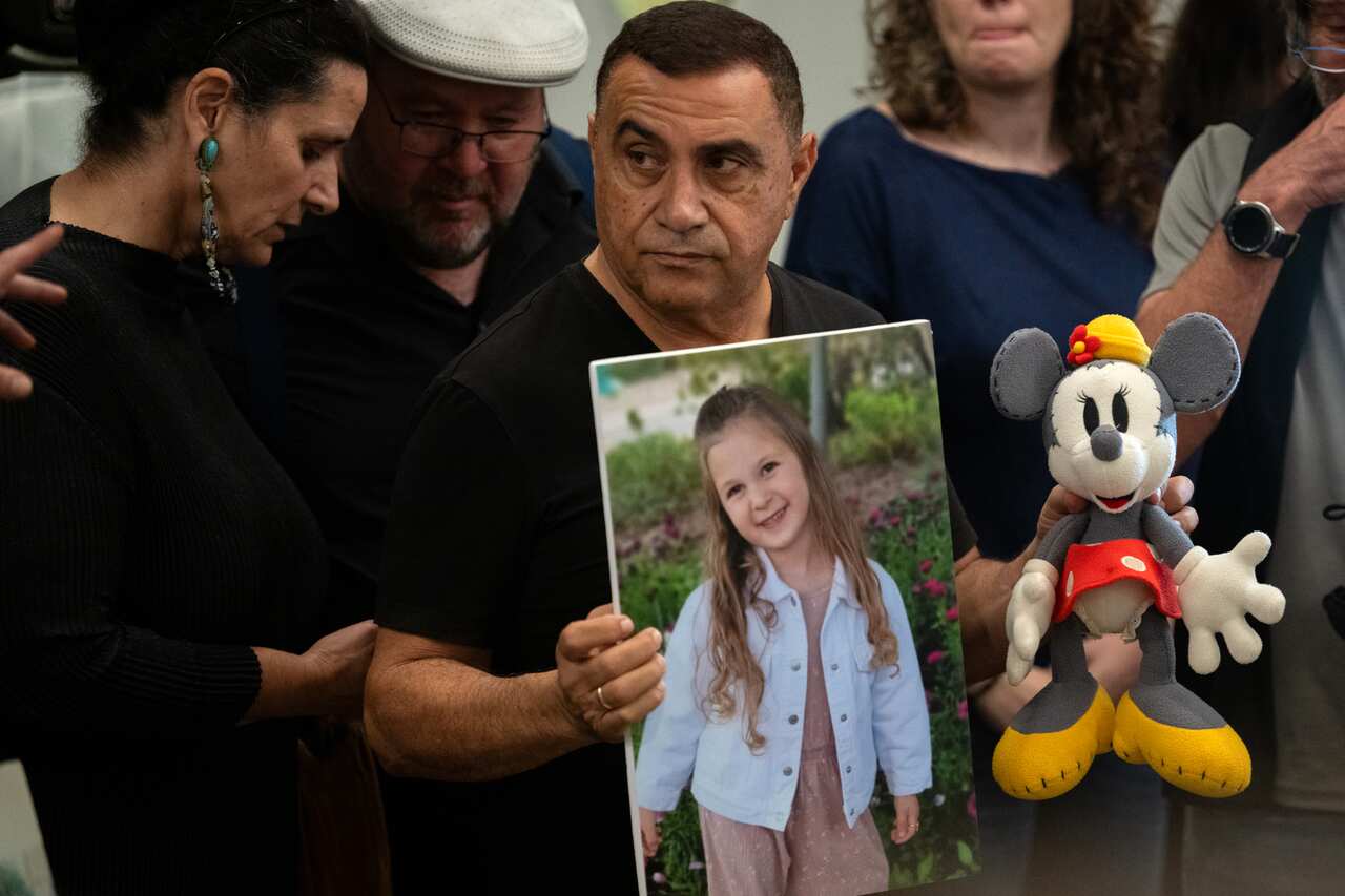 A man holds up a photo of a child and a doll.