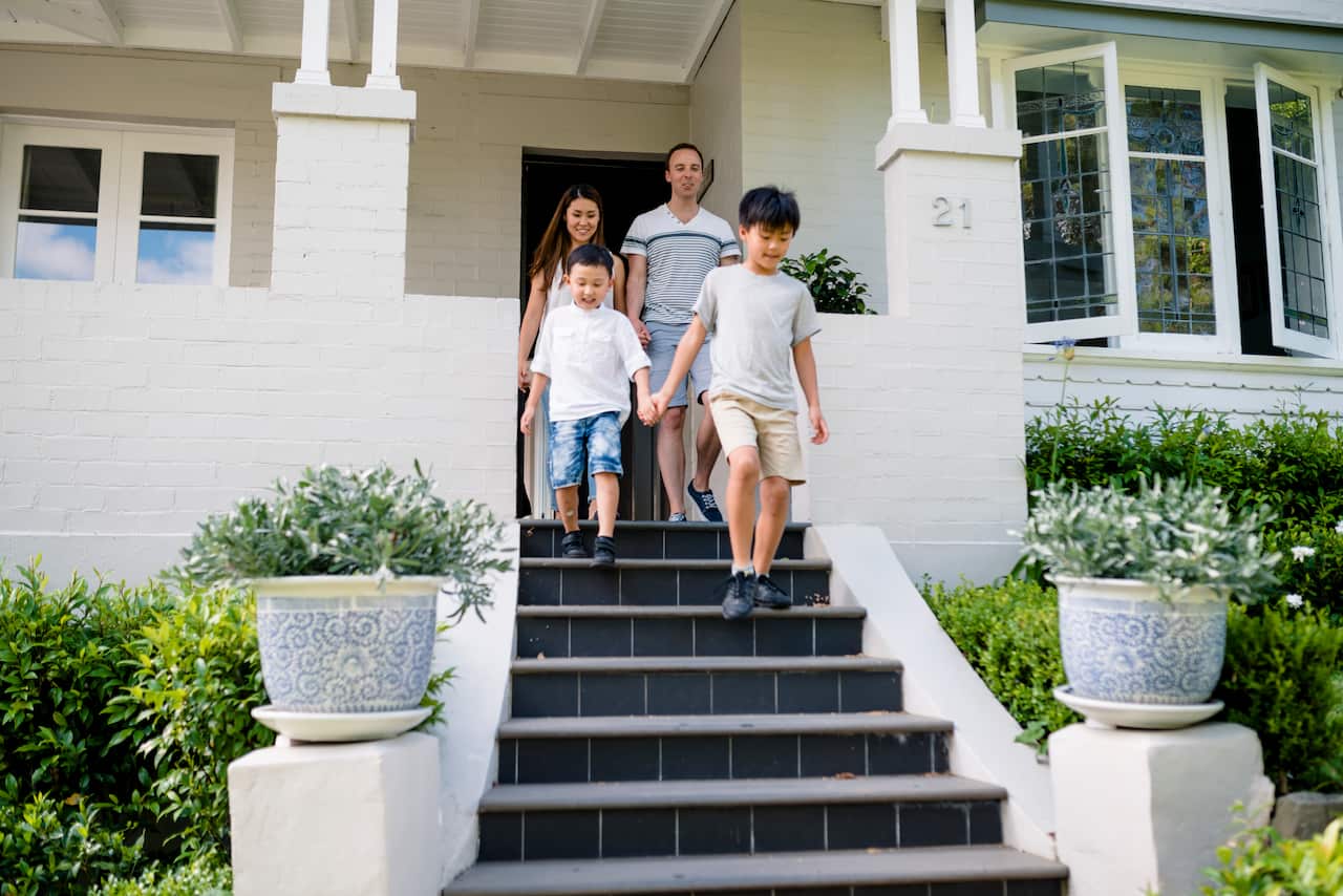 A young family with two small children walks down the stairs of a house