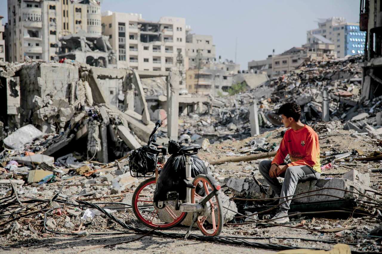 A young man sitting amid the rubble of destroyed buildings in Gaza City