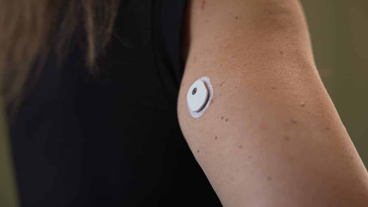 A woman's arm has a little white button stuck to her with a small black hole at the top.