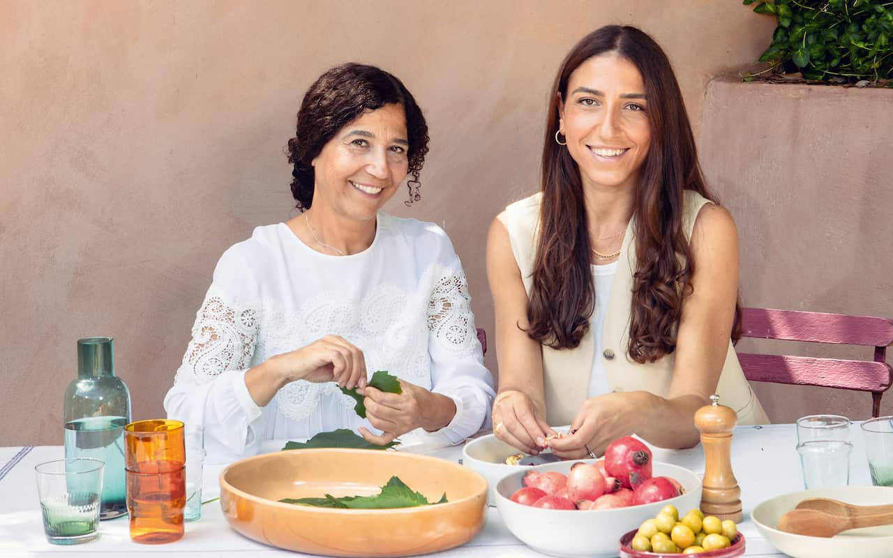Two women sit at an outdoor table, preparing food. 