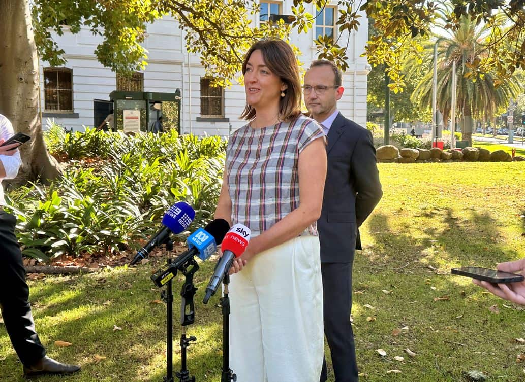 A woman speaking to the media behind some microphones