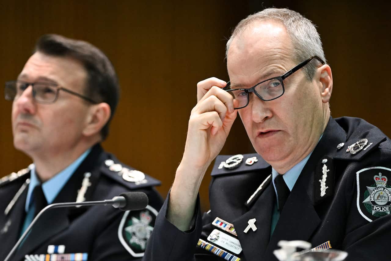 A man in the formal uniform of the Australian Federal Police adjusts his glasses