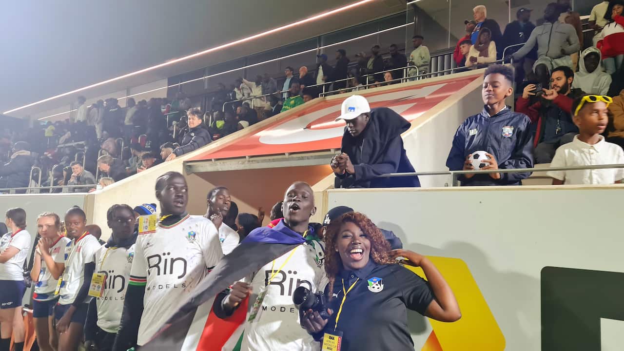 Crowds cheering and smiling at the camera in night time at a stadium.