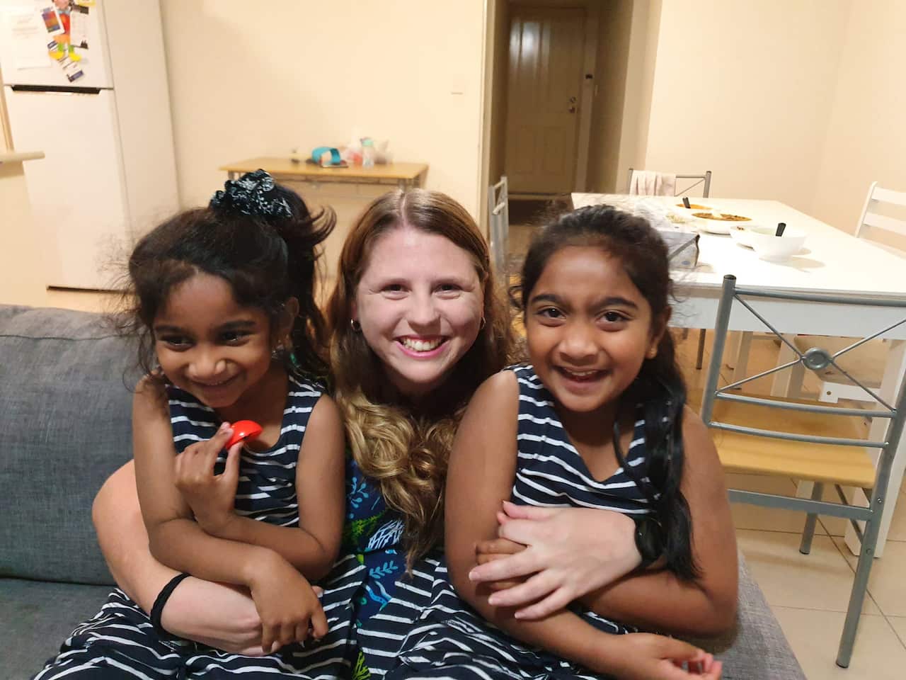 Angela hugs two girls who sit in her lap while all laughing. 