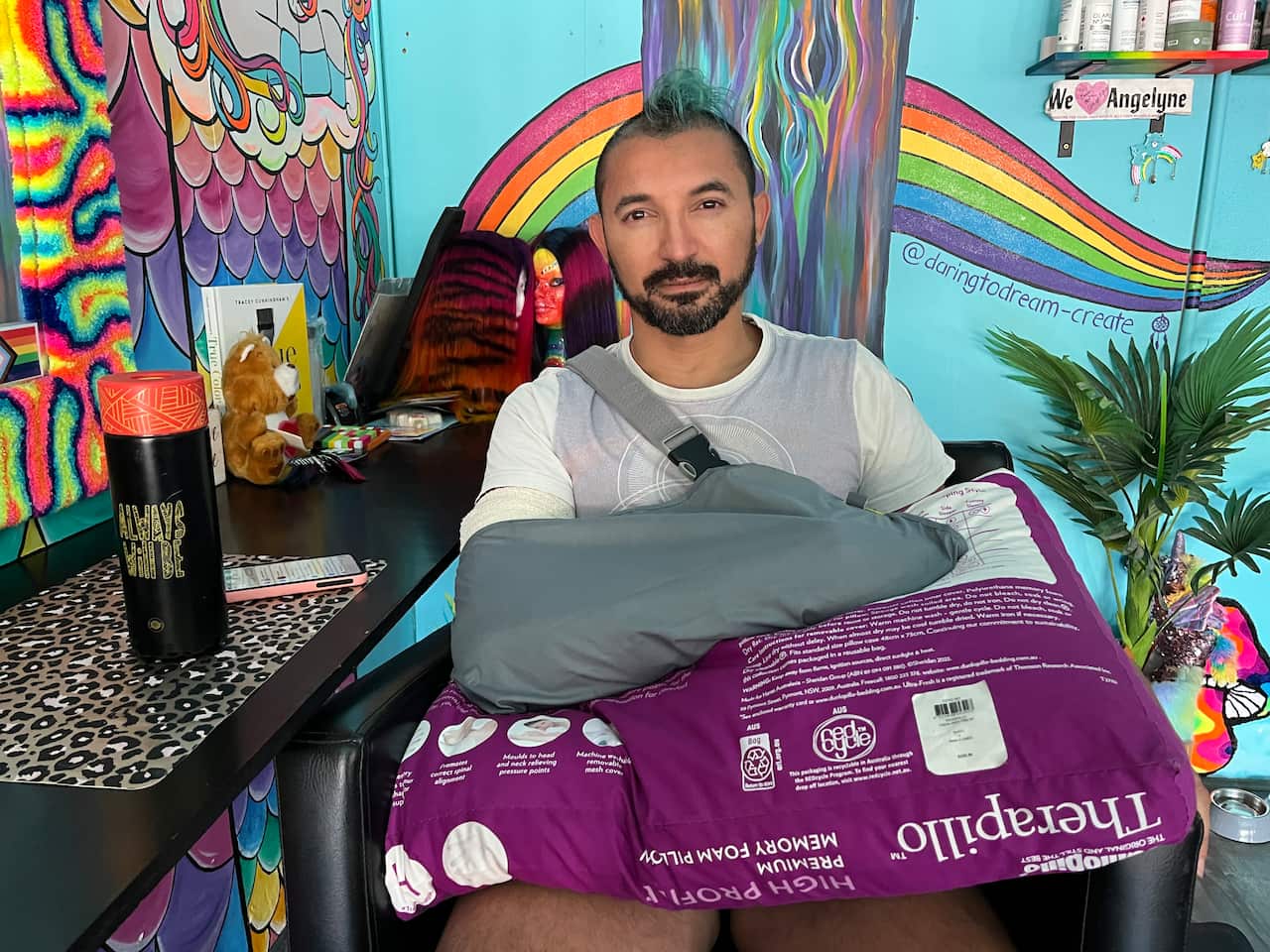 A man sitting down with his arm in a sling resting on a pillow.