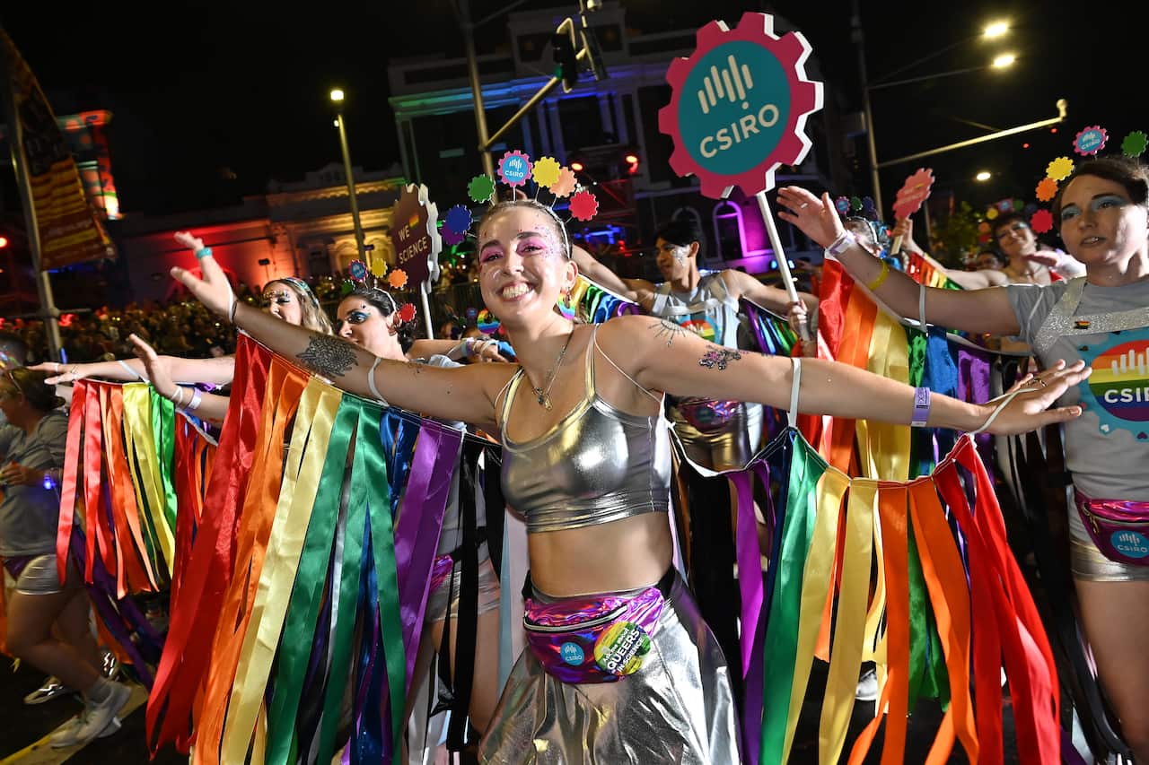 People wearing silver and rainbow outfits with CSIRO signs marching in the Mardi Gras parade