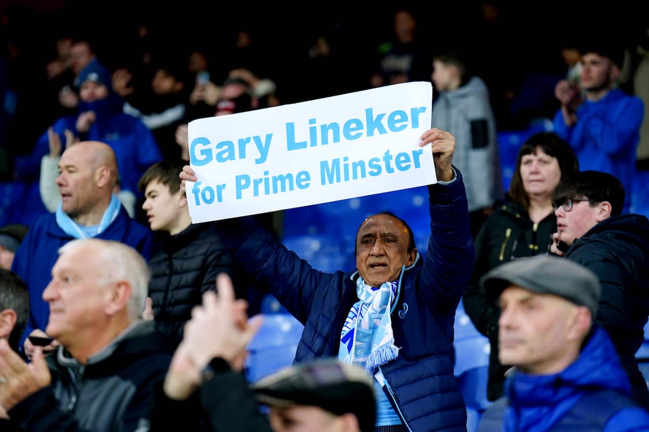 A man holds a sign that reads: "Gary Lineker for prime minister" at a football game. 