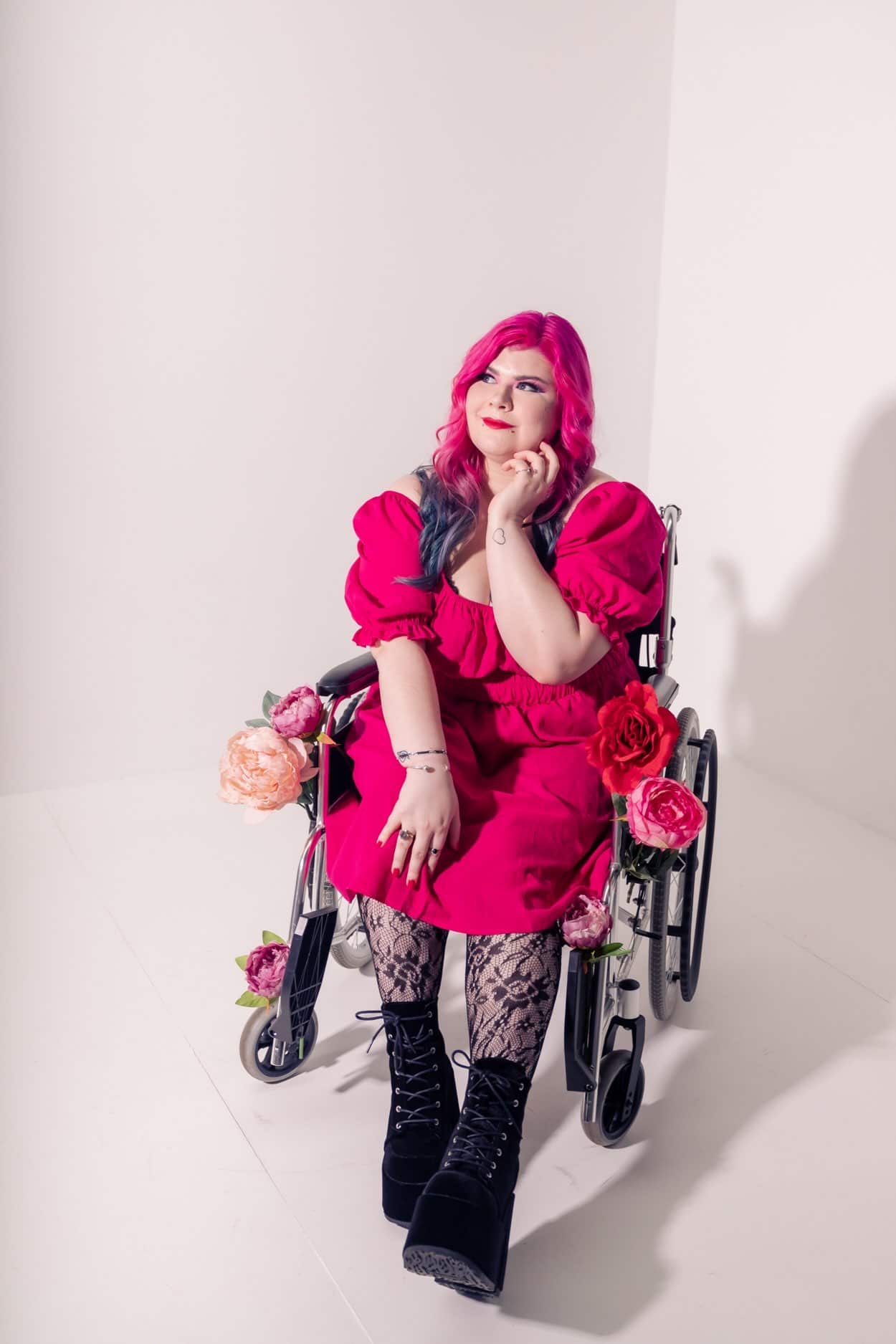 A picture of Zoe Simmons wearing a pink dress and sitting in her wheelchair, which is adorned with flowers. 