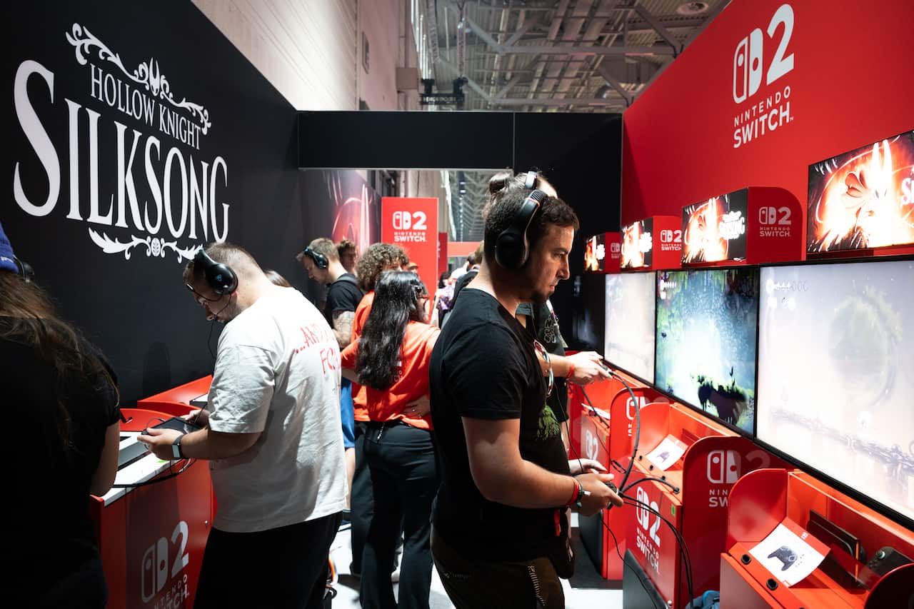 People playing video games on machines. One board says "Hollow Knight: Silksong" while another says "Nintendo Switch 2".