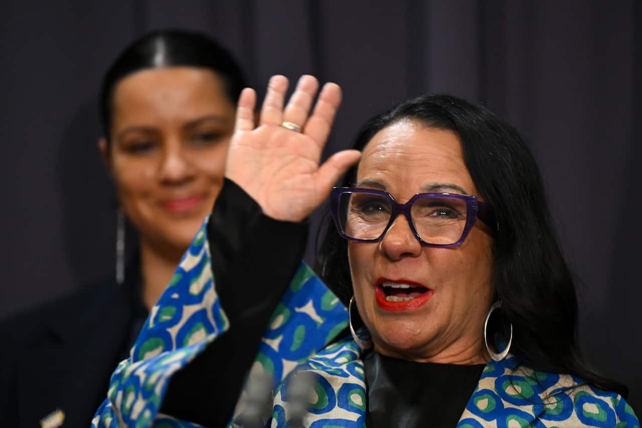 Woman in glasses waves.