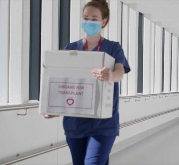 A woman in medical scrubs carries a box with a label that reads: Organs for Transplant.