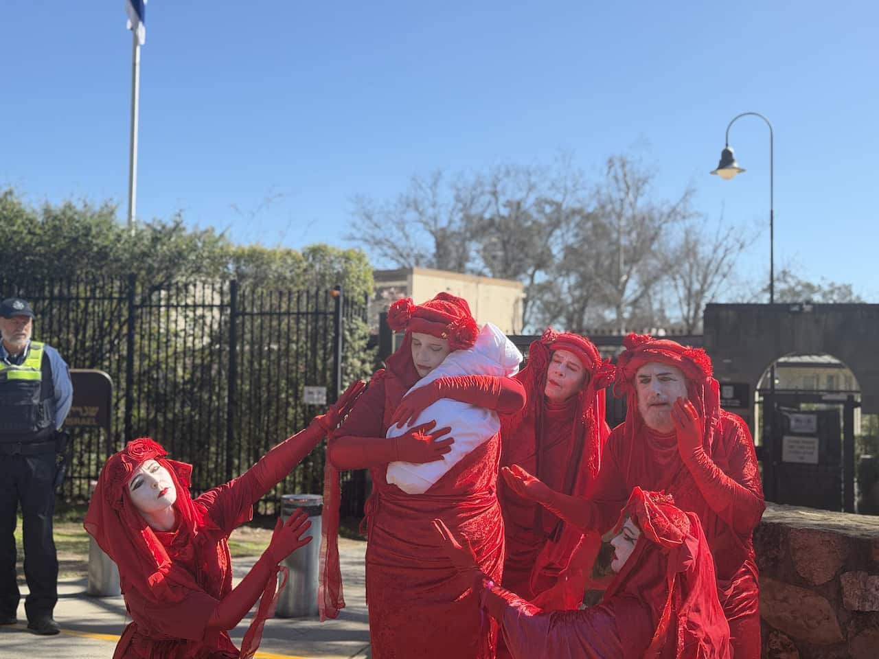 Protesters wearing red holding a white bundle in the shape of a baby