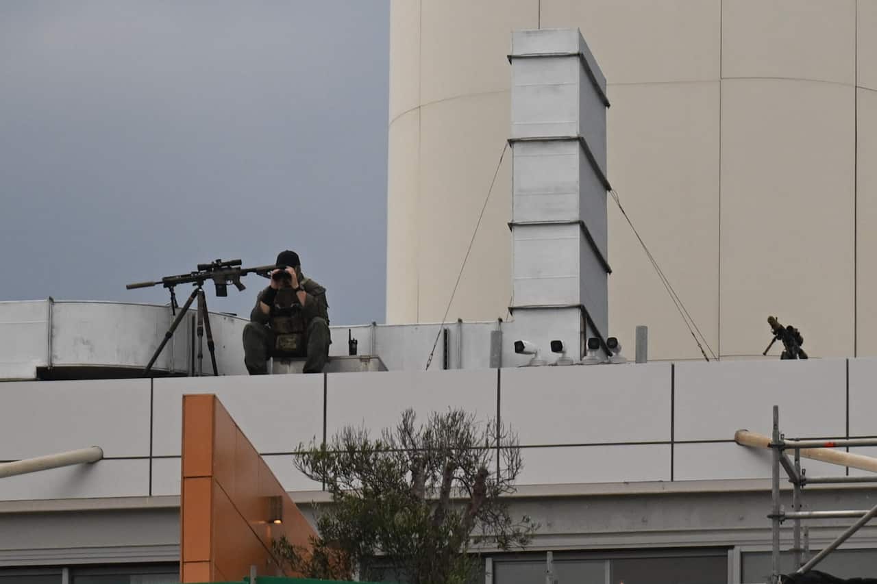 A police sniper looks through binoculars from atop a building.