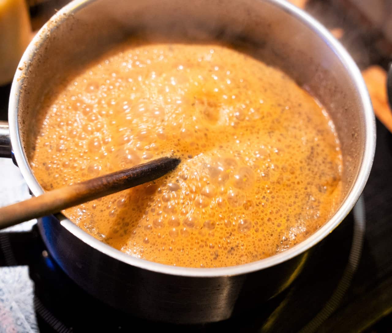 A silver pot filled with golden milk and spice sits boiling on a stovetop.
