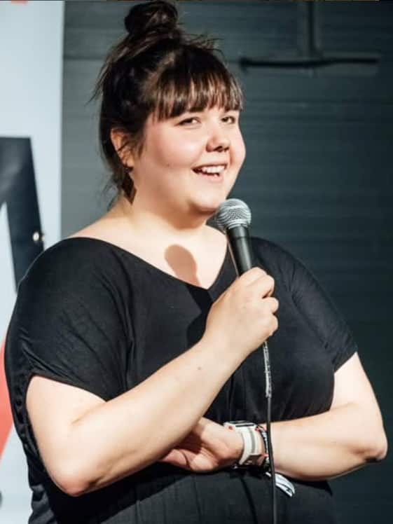 A person wearing a black top is standing on stage, holding a microphone.