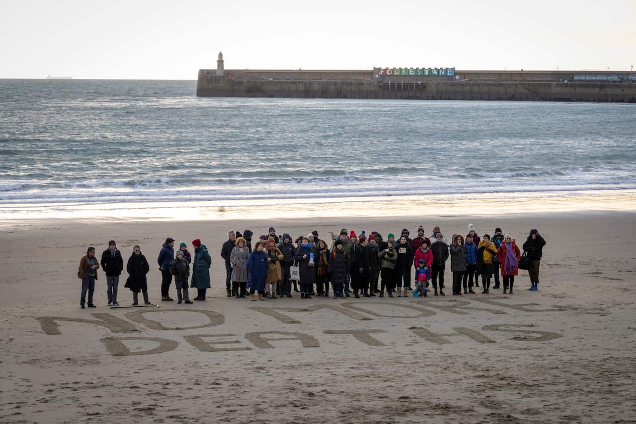 A group of people standing on a beach. They have written "NO MORE DEATHS" in the sand.