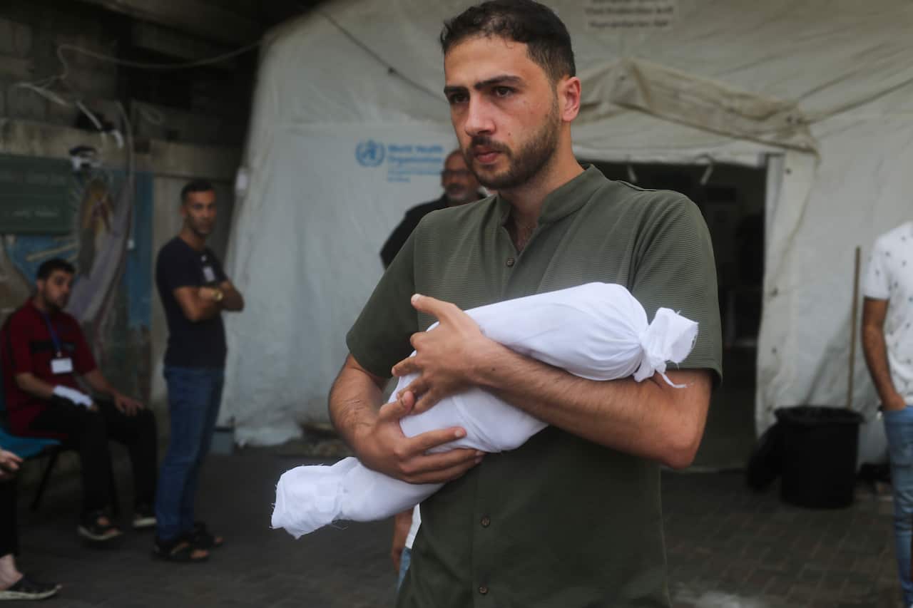 A man carries the body of a baby wrapped in a shroud