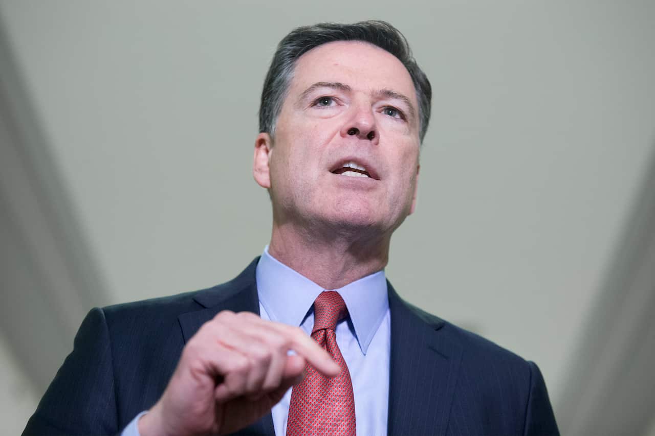 A man in a dark blue suit, light blue shirt and red tie. His hand is raised.