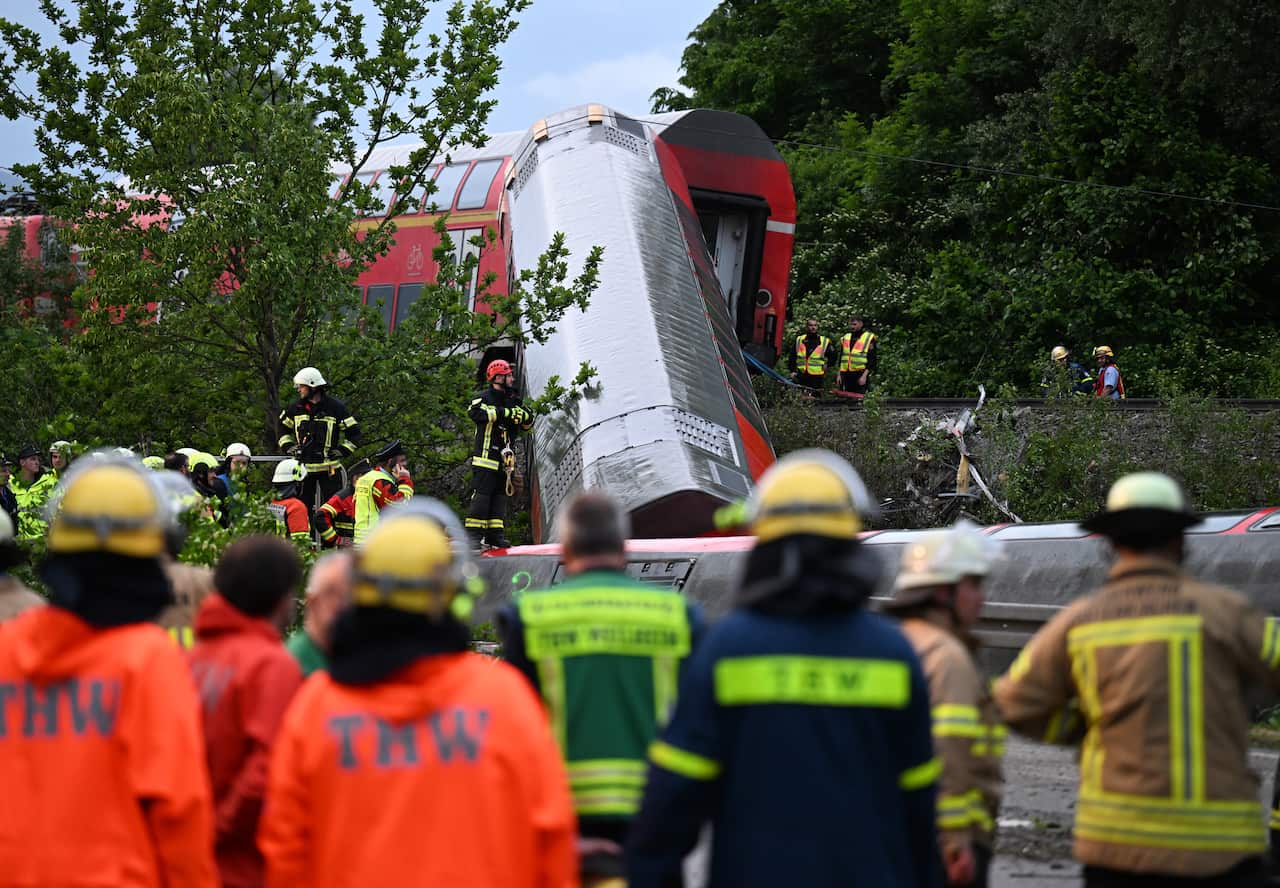 Several rescue workers can be seen with their backs to the camera near the site of a train crash.