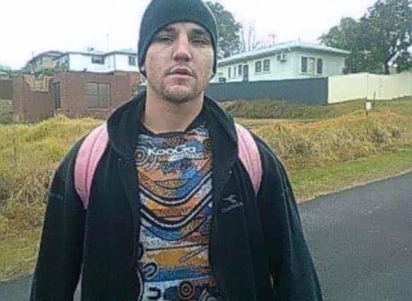 A young man wearing a hoodie beanie and backpack standing on a footpath