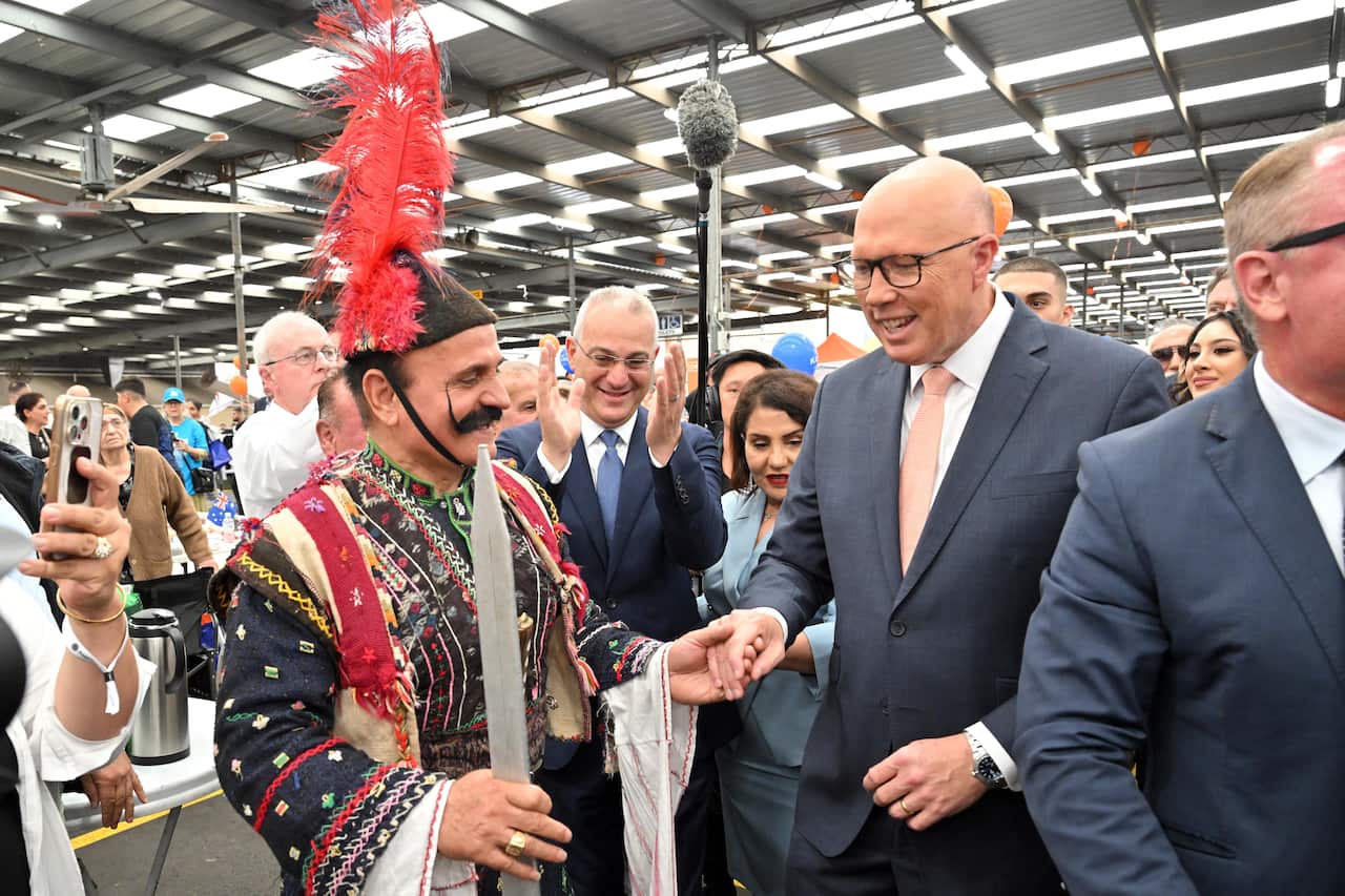 Peter Dutton at a community event, surrounded by others, and holding the hand of someone in traditional dress.