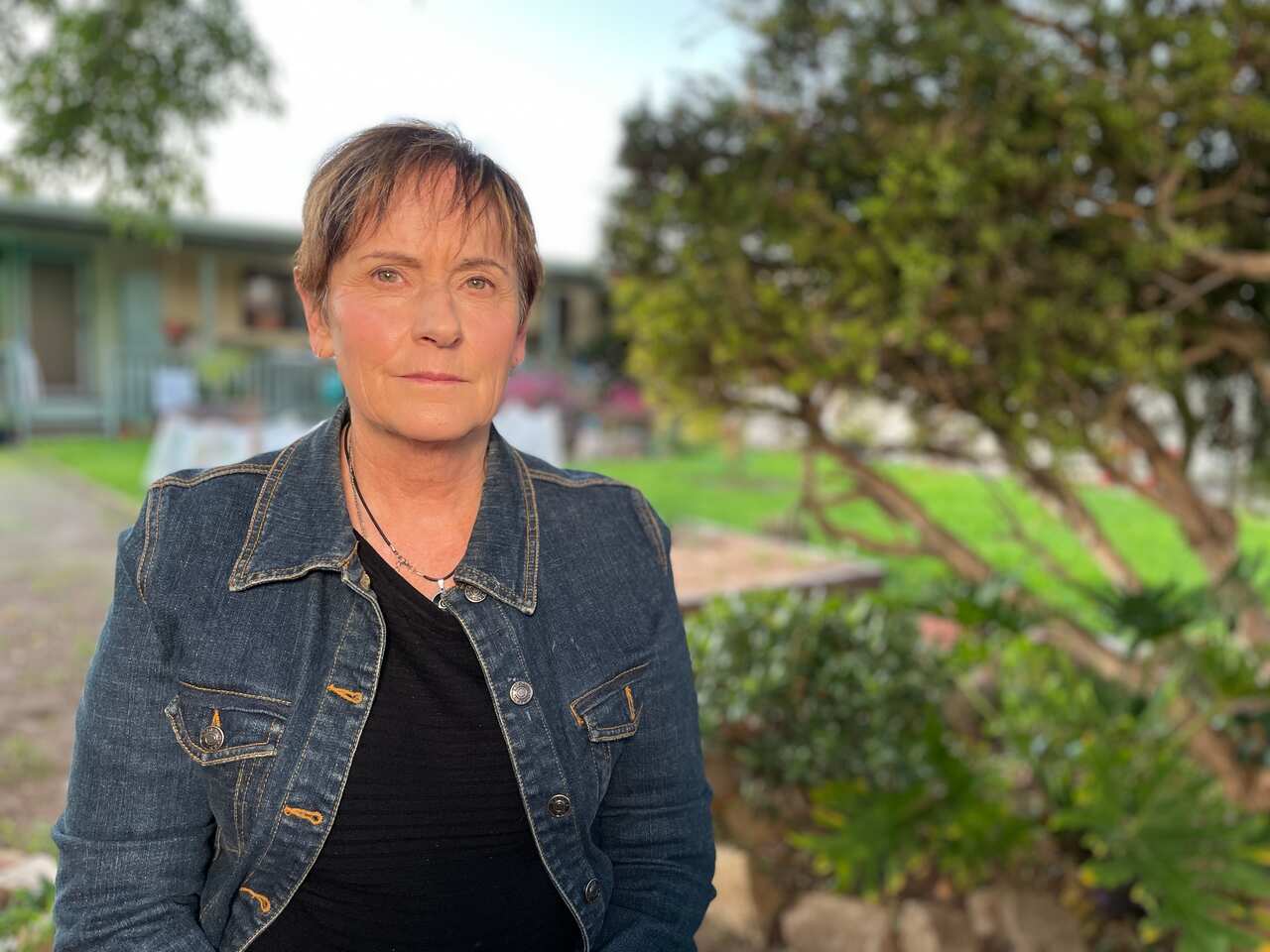A woman in a denim jacket outside with a serious expression 