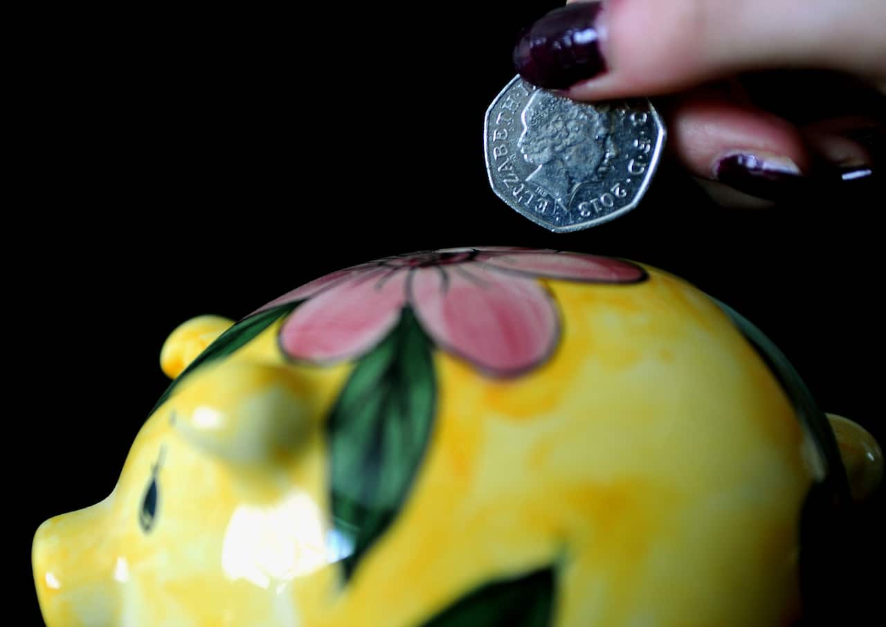 A hand deposits a fifty cent coin into a yellow piggy bank with pink flowers.