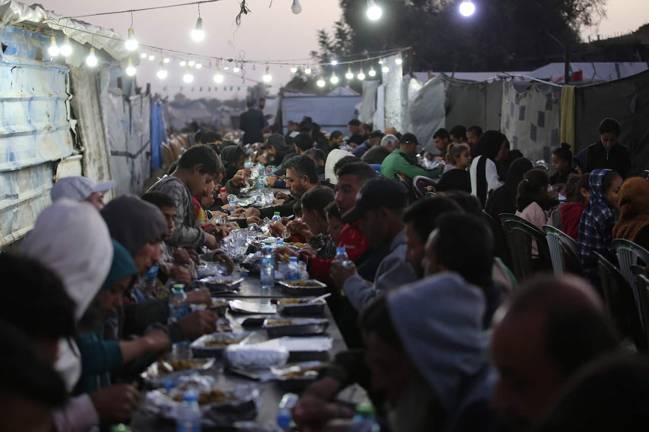 People sit crowded around long tables while eating.