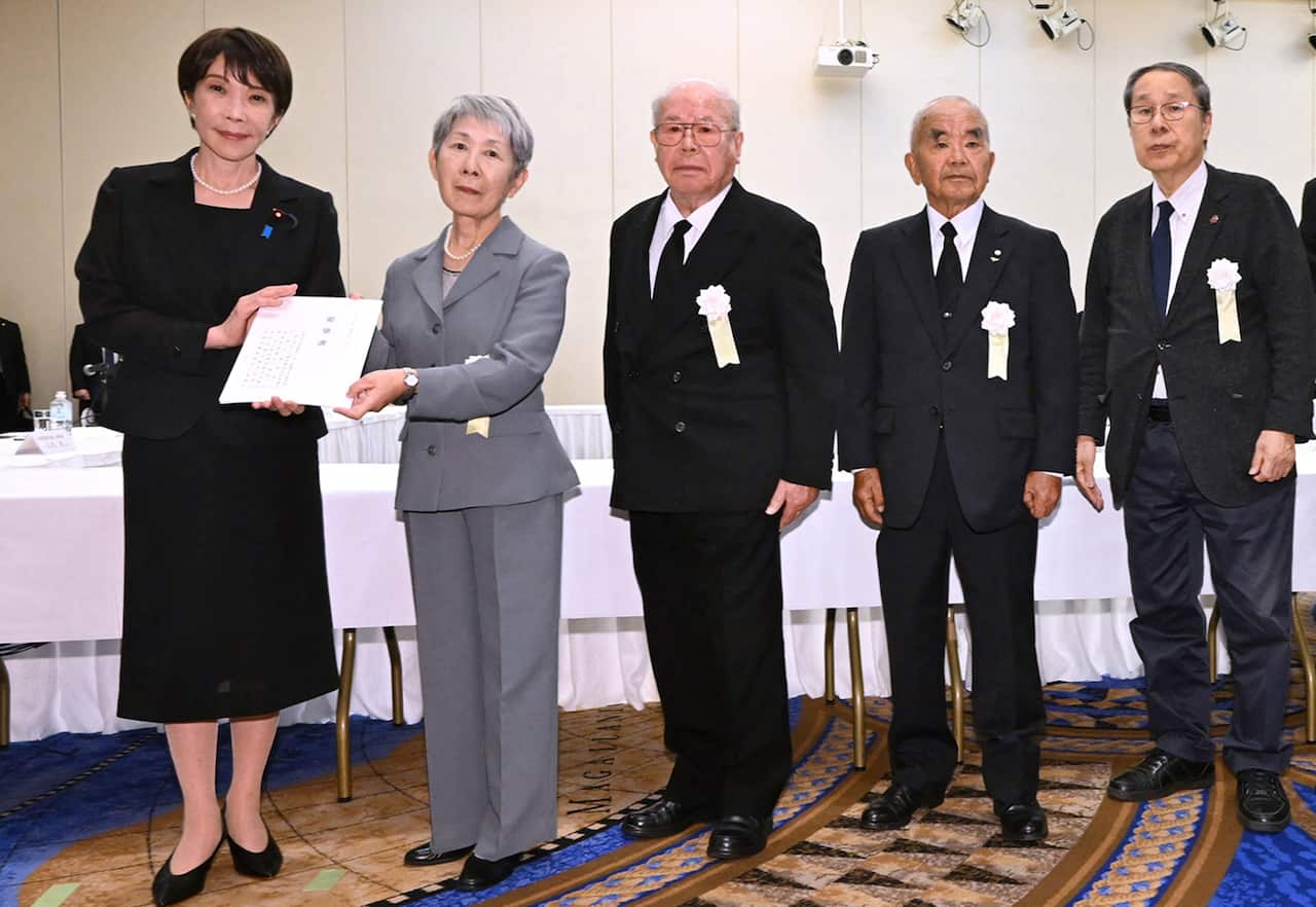 Japanese Prime Minister Sanae Takaichi holds a written request from atomic bomb survivors standing to her right.