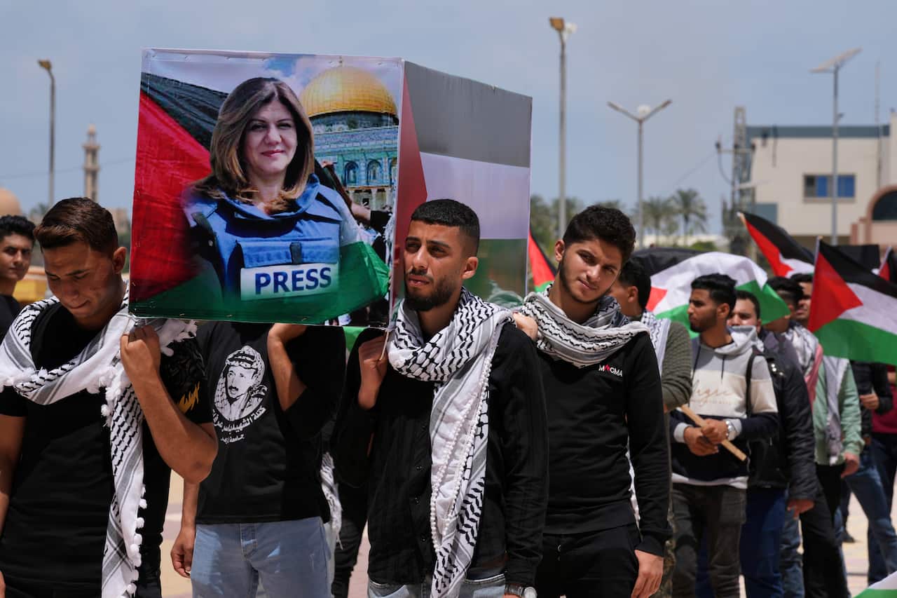 Young men carry a large photo of a woman wearing a vest with the word "PRESS" on it.