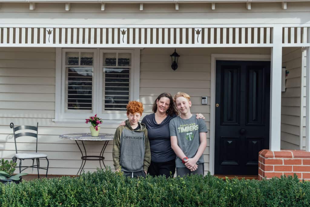 A woman and two boys standing outside a house