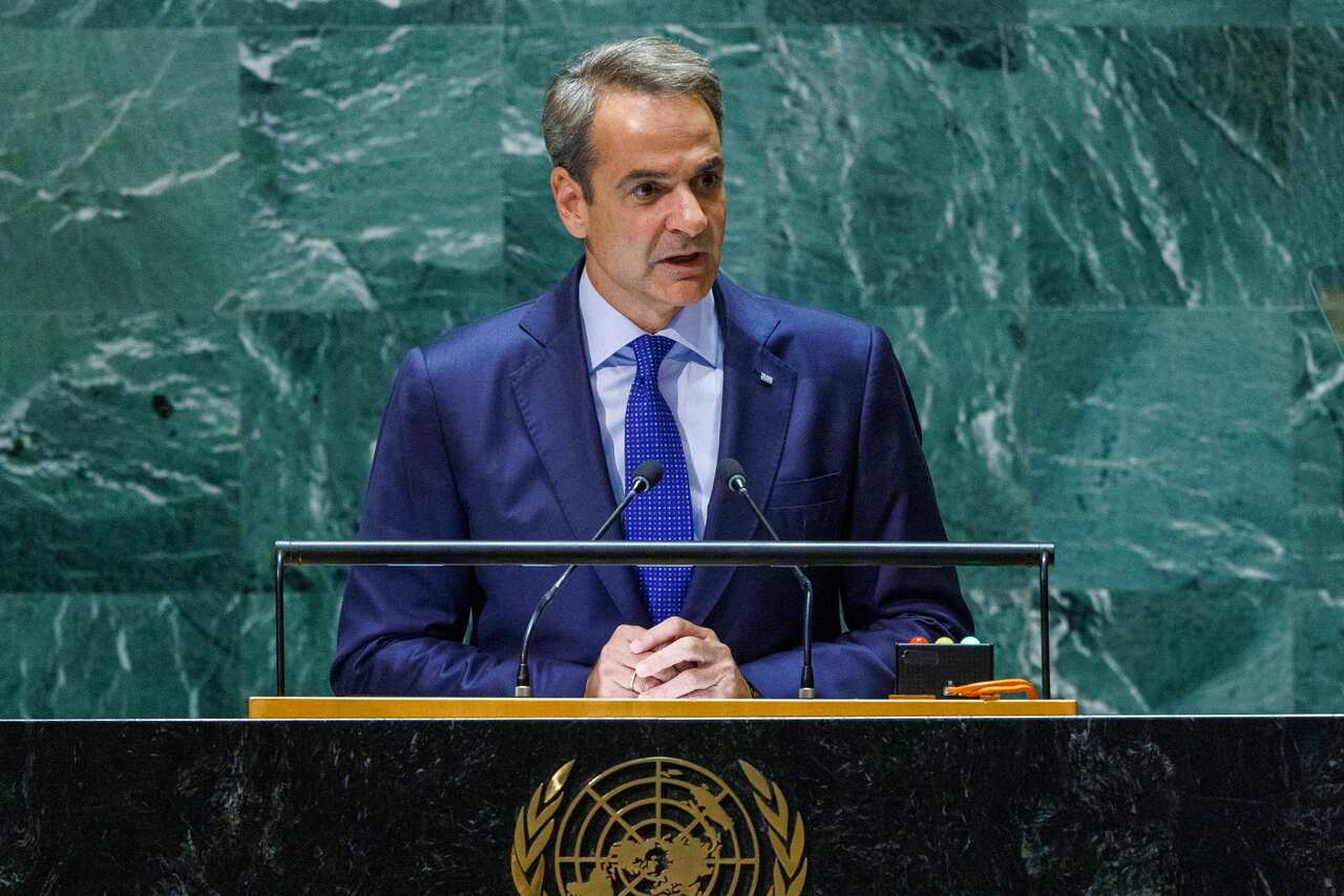 Greek Prime Minister Kyriakos Mitsotakis standing on a podium delivering a speech.
