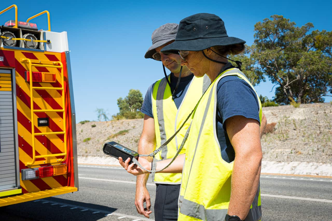 People looking at a gauge while standing on the side of a road.