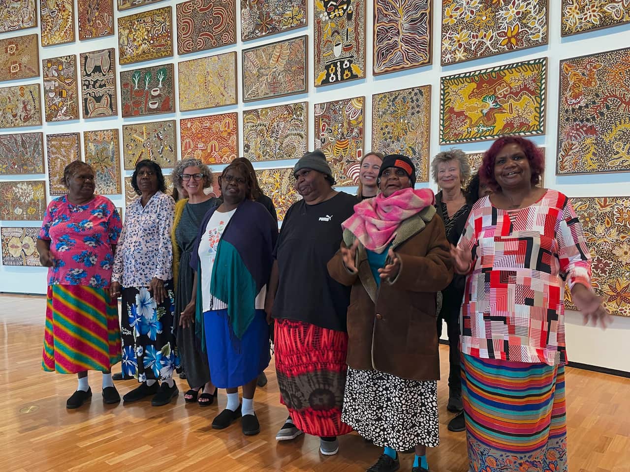 The opening of the Emily Kam Kngwarray exhibition NGA December 2023 The work behind is "A Summer Project: Utopia Women's Paintings” 1988/89. L-R, Front Row: Jean Kngwarray Long, Margaret Kngwarray Long, Kelli Cole, Louisa Kngwarray Long, Jedda Kngwarray Purvis. L-R, Back Row: Sophia Lunn, Dr Jennifer Green. Front Row: Josie Petyarr Kunoth, Melissa Kngwarray Long.