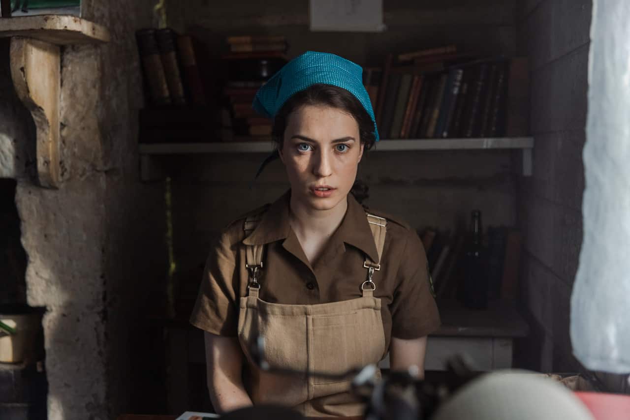 A woman in workers overalls sits in a cottage