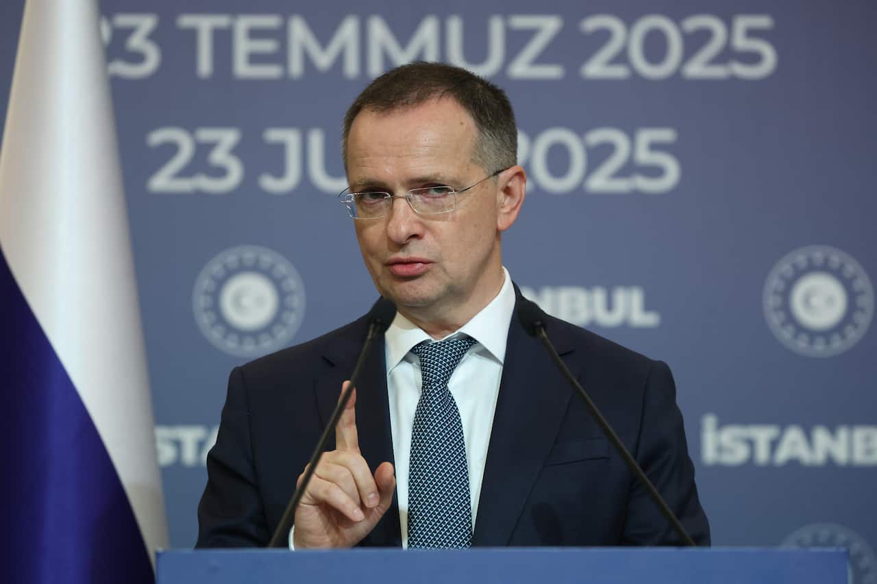 A man wearing a suit and glasses speaking at a lectern. 