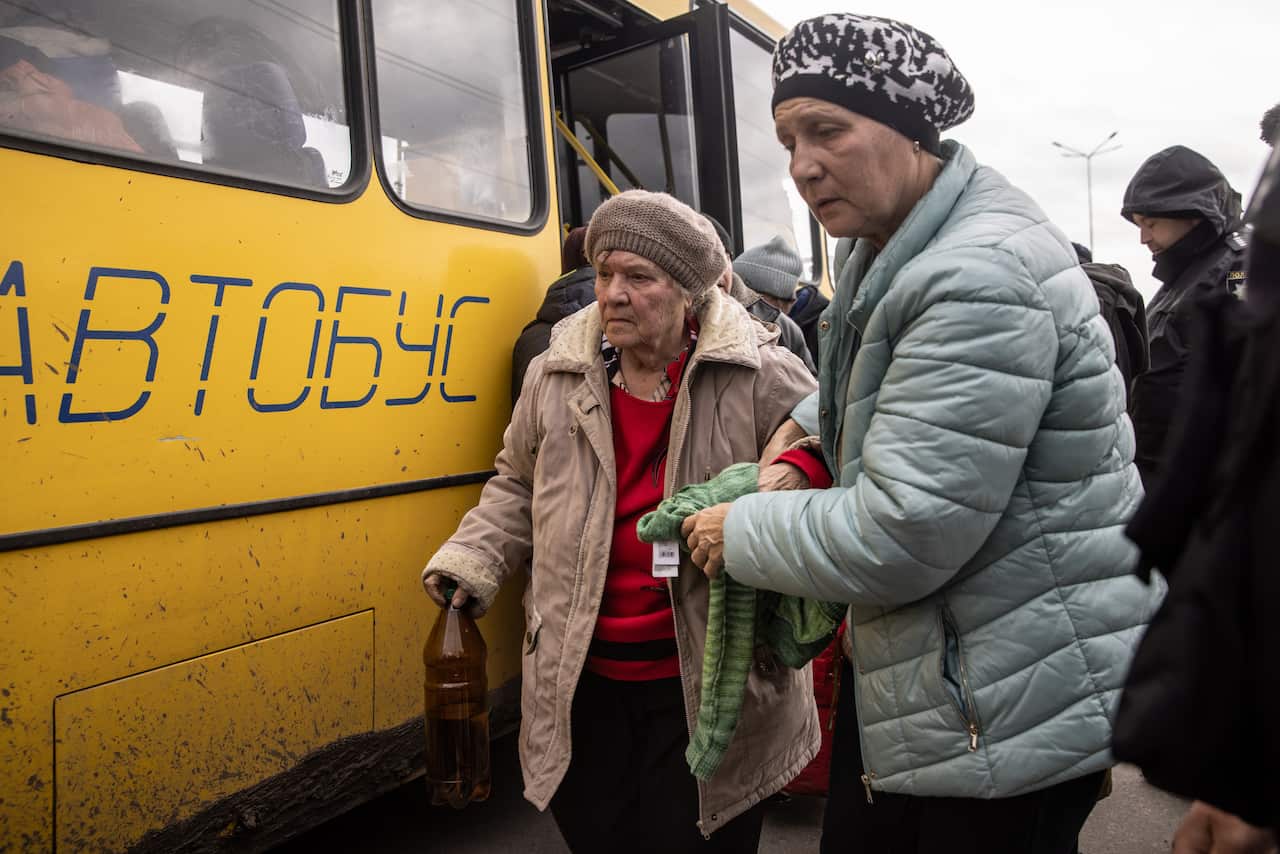 Two women get off a bus wearing layered clothing and warm hats. 