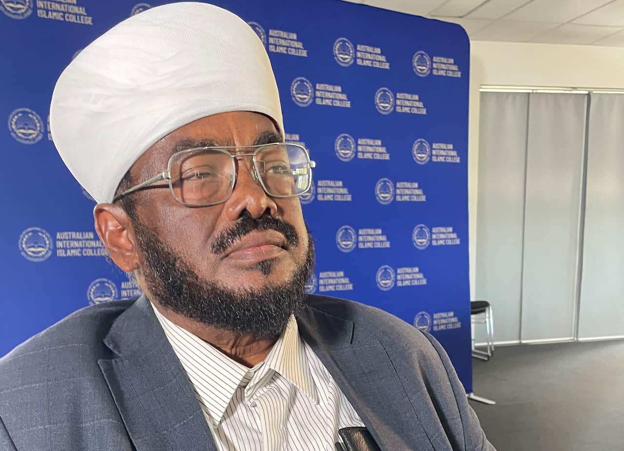 A man with glasses and white hat and wearing a suit jacket 