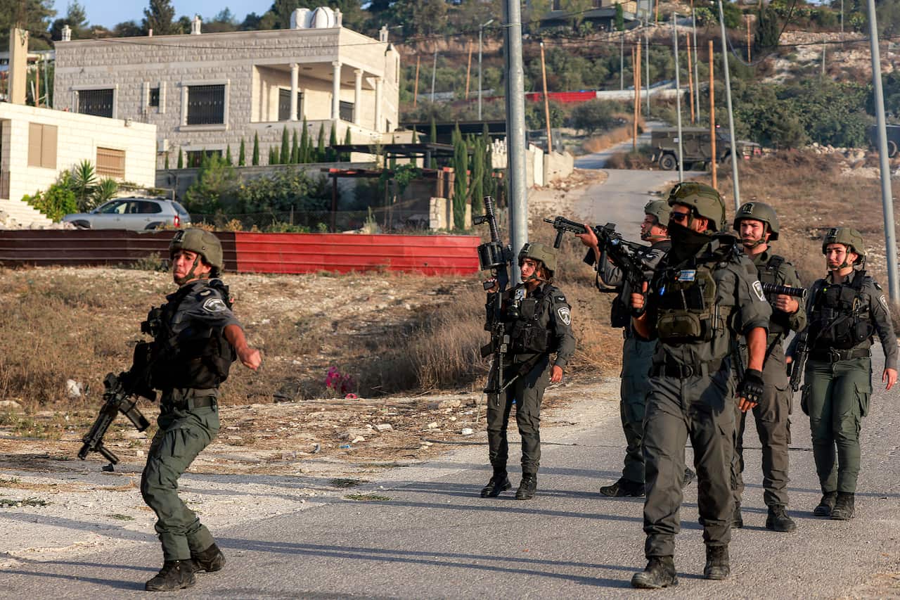 Soldiers patrol a street with a house seen in the background