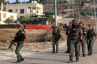 Soldiers patrol a street with a house seen in the background