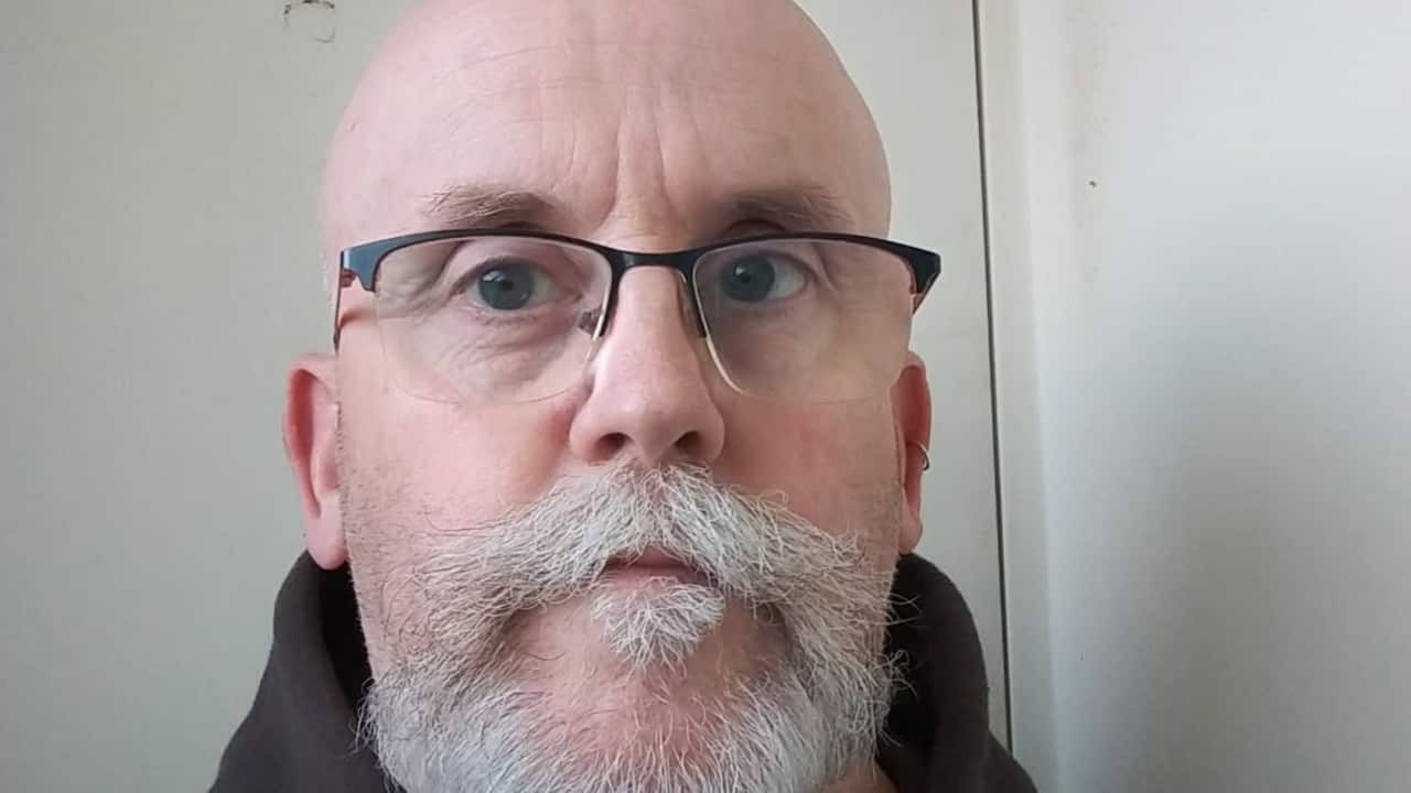 a close up photo of an older man with a bald head and white beard and wearing glasses
