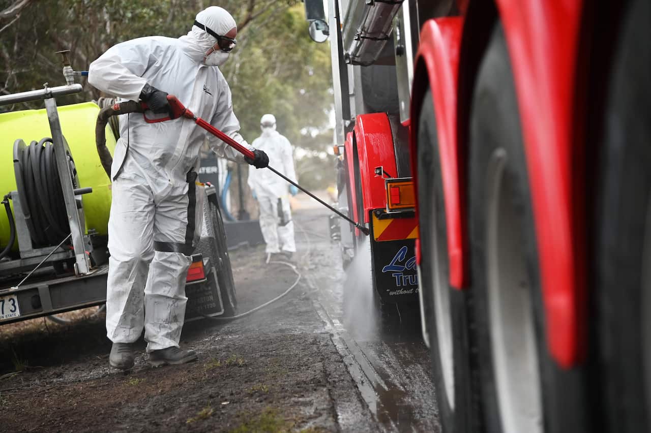 A person in a hazmat suit hoses down the wheels of a truck