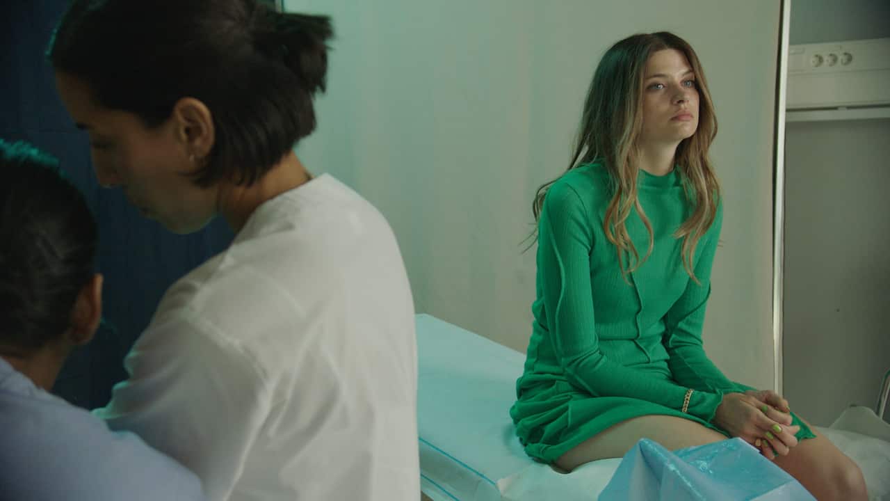 A young woman sits forlorn on a hospital bed.png