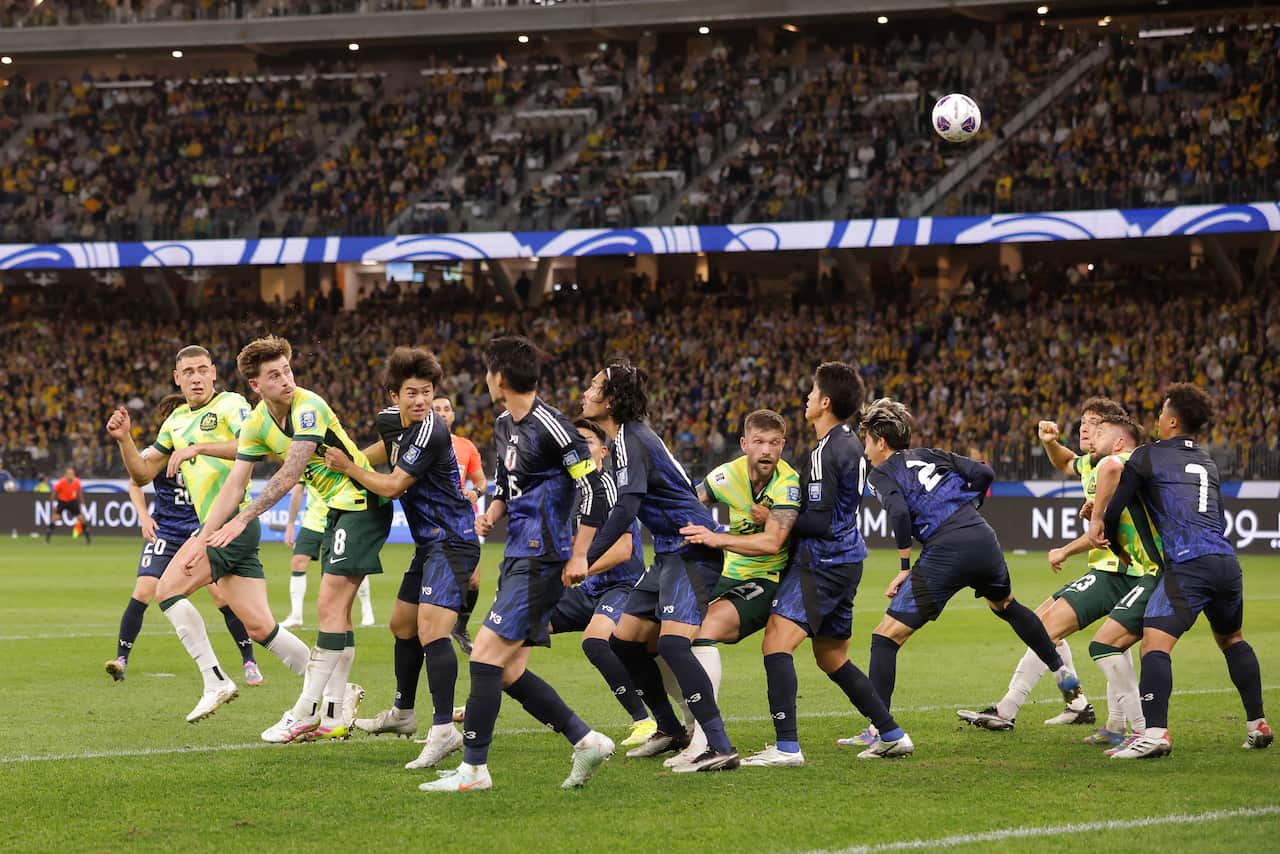 Football players in green and blue jerseys are on the playing field during a match.