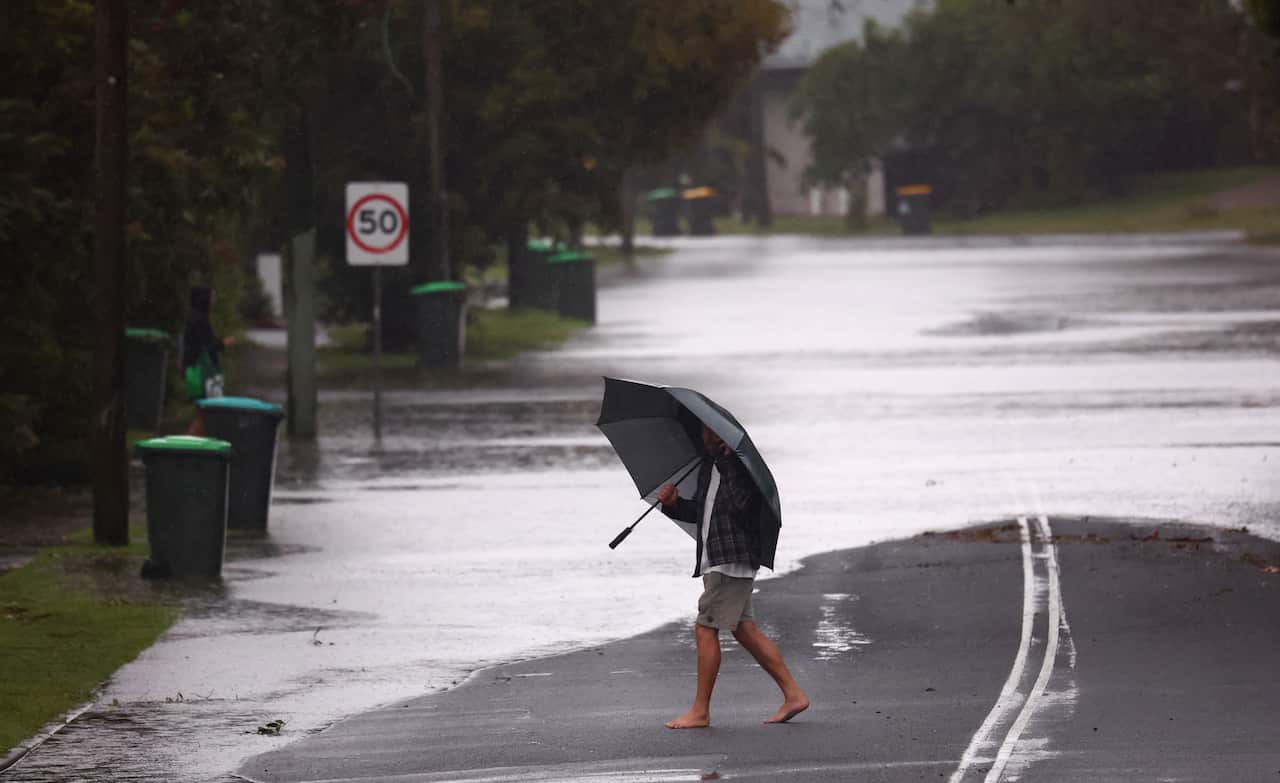 A man with an umbrella walking in front of a flooded road